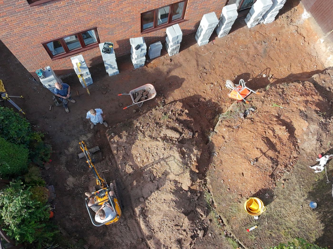 Trio Construction Group groundworkers excavating a rear garden in Solihull, with a mini digger and materials set out on site